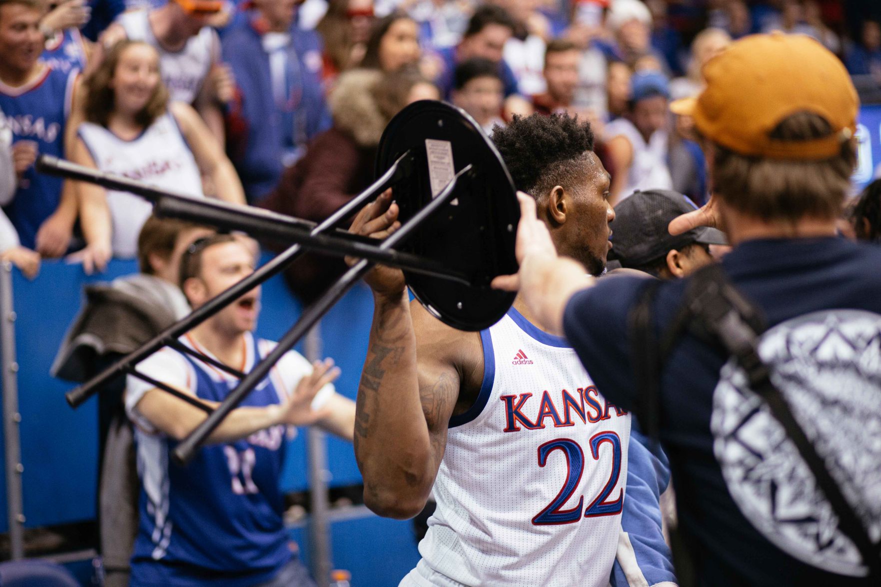 Silvio De Sousa holds a chair above his shoulder during a fight behind the basket.